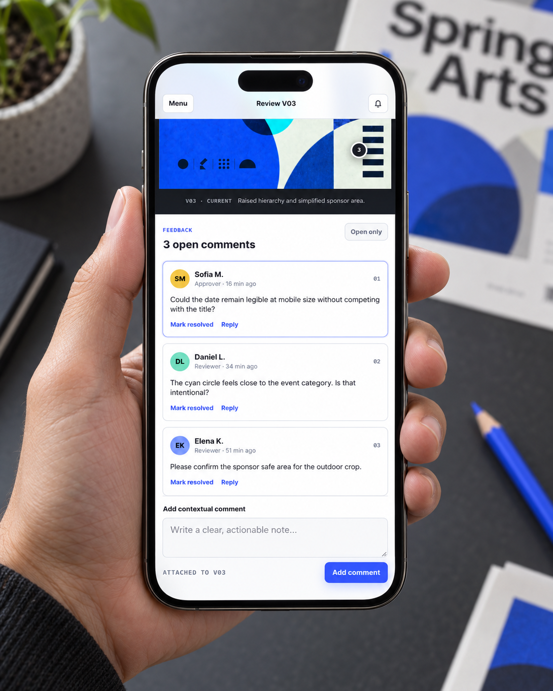 Revision Room contextual comments displayed on a smartphone held above a creative workspace
